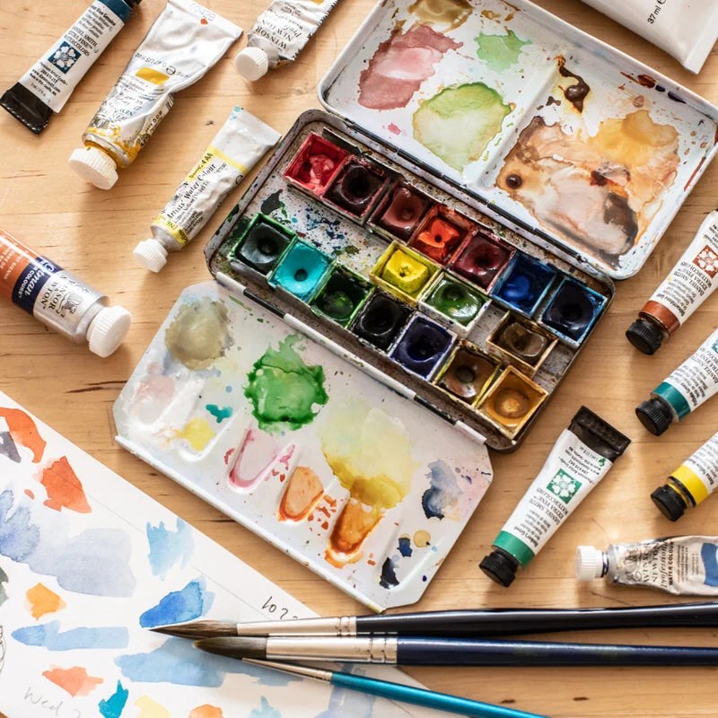 Acuarelas, pinceles y tubos de pintura sobre una mesa de madera