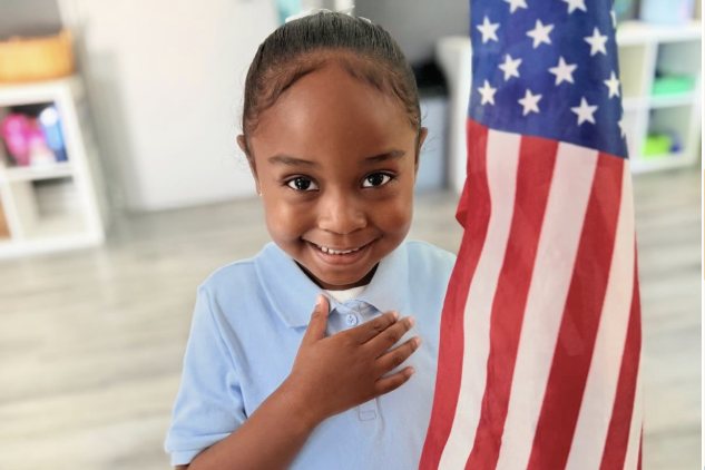 Niña con la mano en el corazón junto a la bandera de Estados Unidos