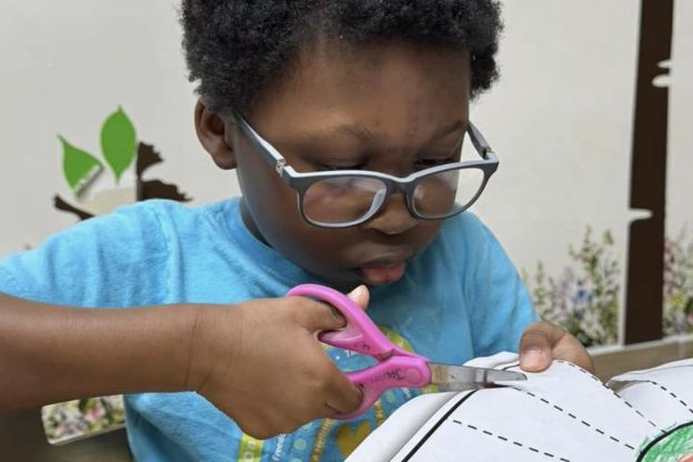 Niño con lentes recortando papel con tijeras de seguridad
