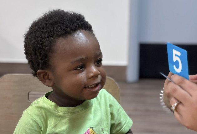 Niño sonriendo mientras aprende el número 5 con una tarjeta